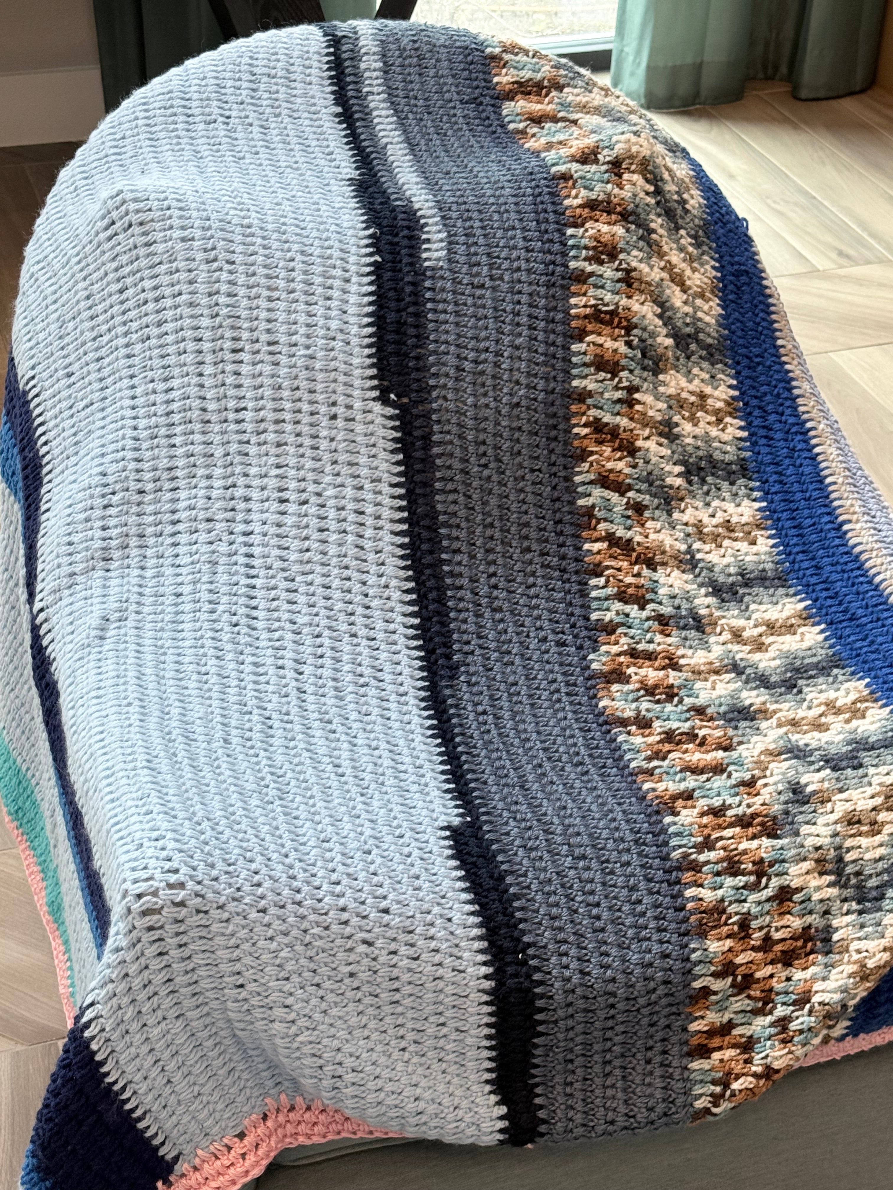 Close-up of multicolor hand crocheted boho blanket showing blue, navy, and pink stitch detail"